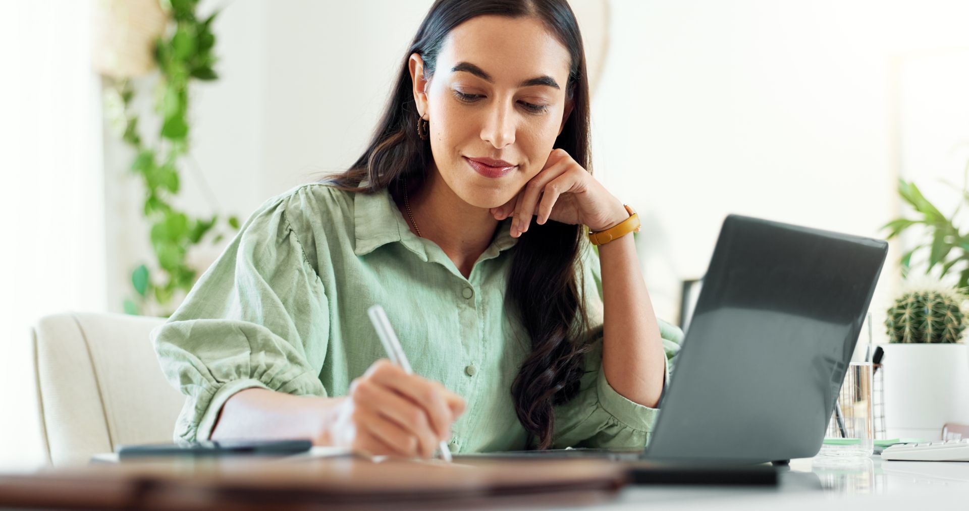 Junge Frau mit Stift und Laptop am Arbeiten am Schreibtisch