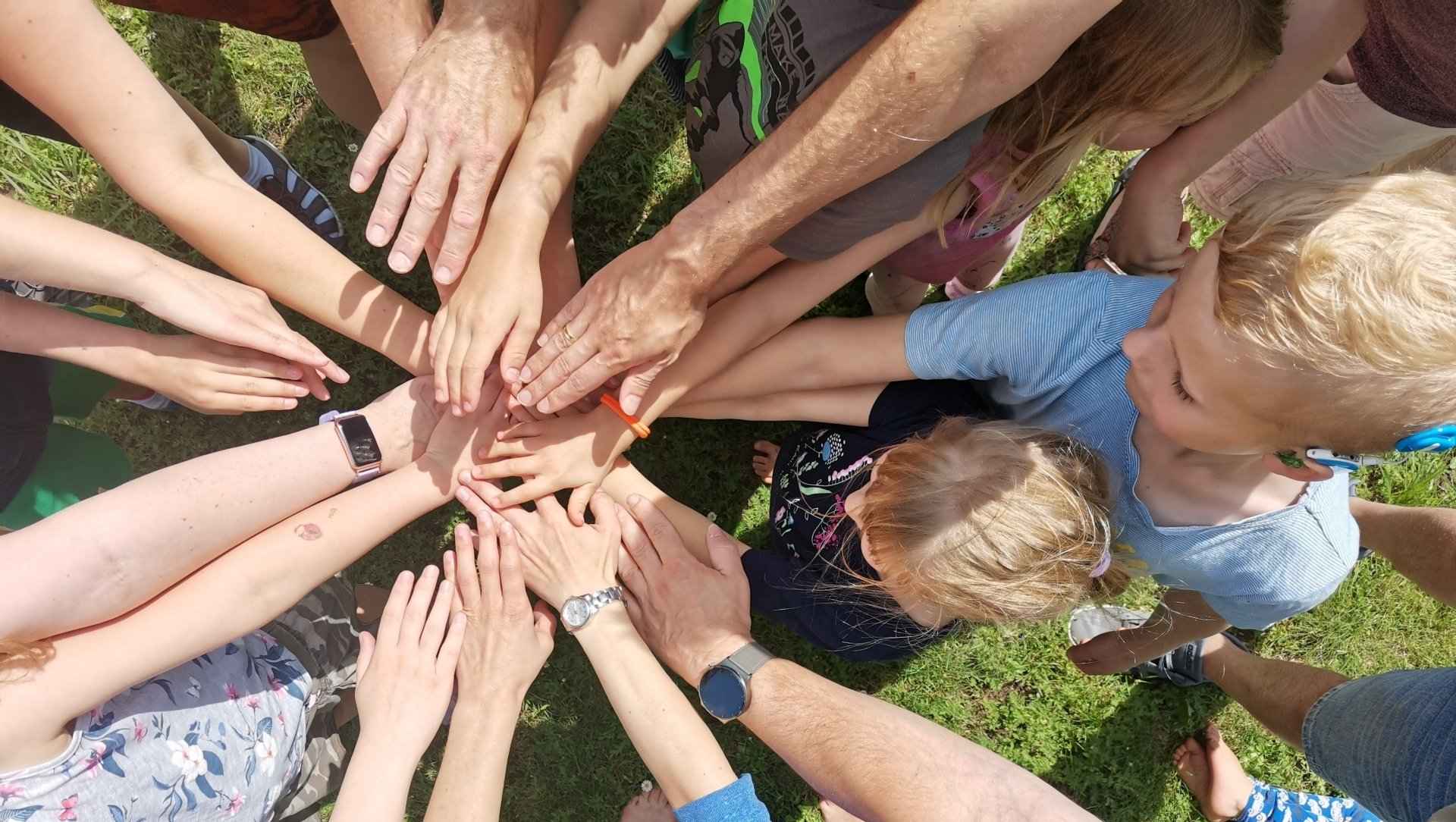 Eltern und Kinder mit Hörbehinderung und Geschwiterkinder legen ihre Hände übereinander als Symbol für ein gemeinsames Netzwerk