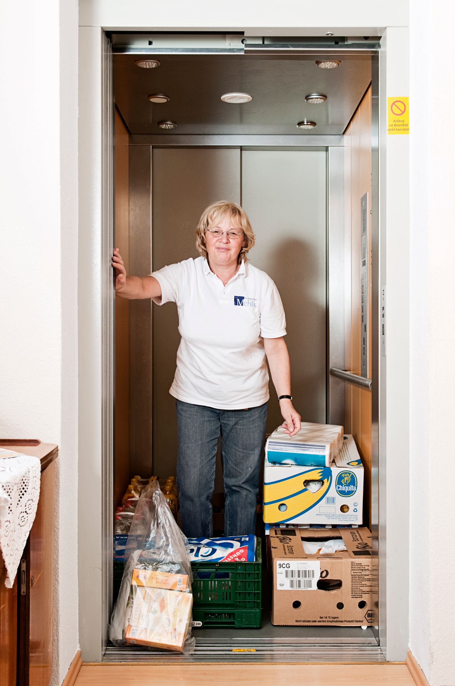lächelnde Mitarbeiterin mit Großeinkauf im Fahrstuhl