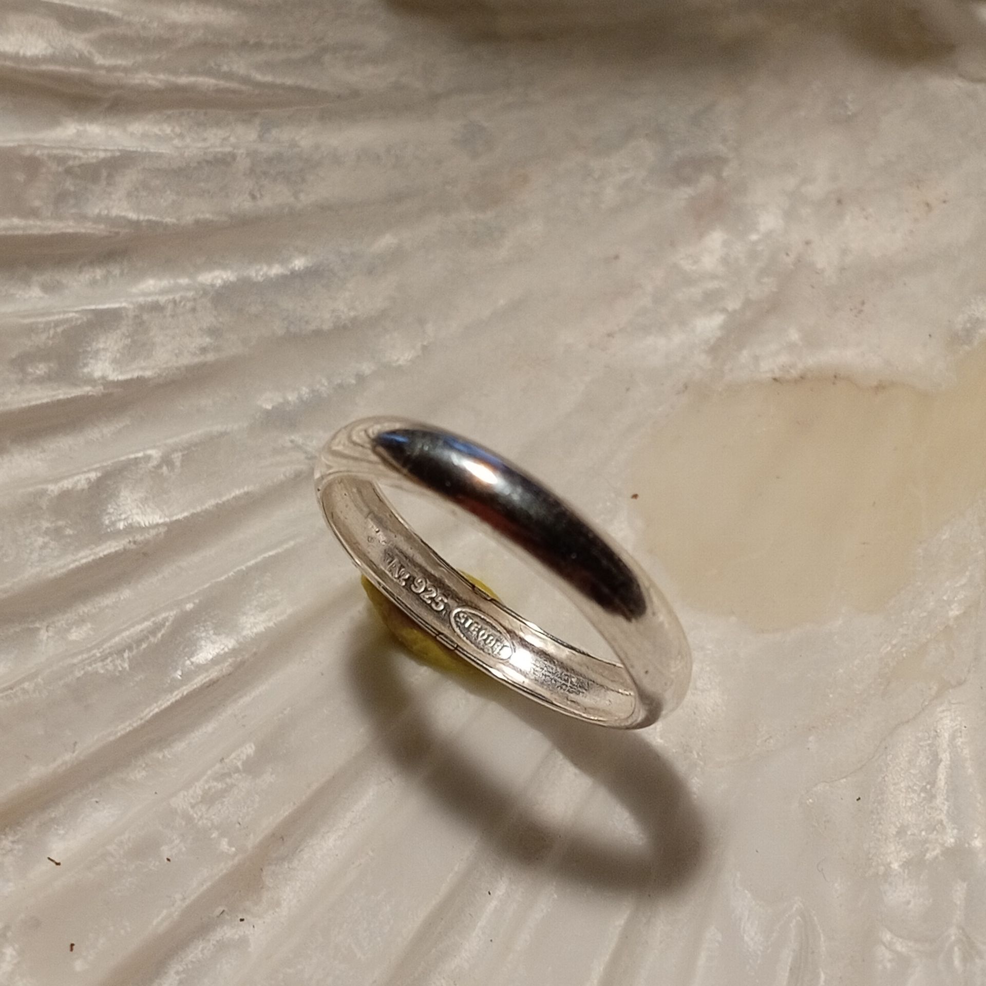 Ein silberner Ring liegt auf einer strukturierten, weißen Oberfläche.