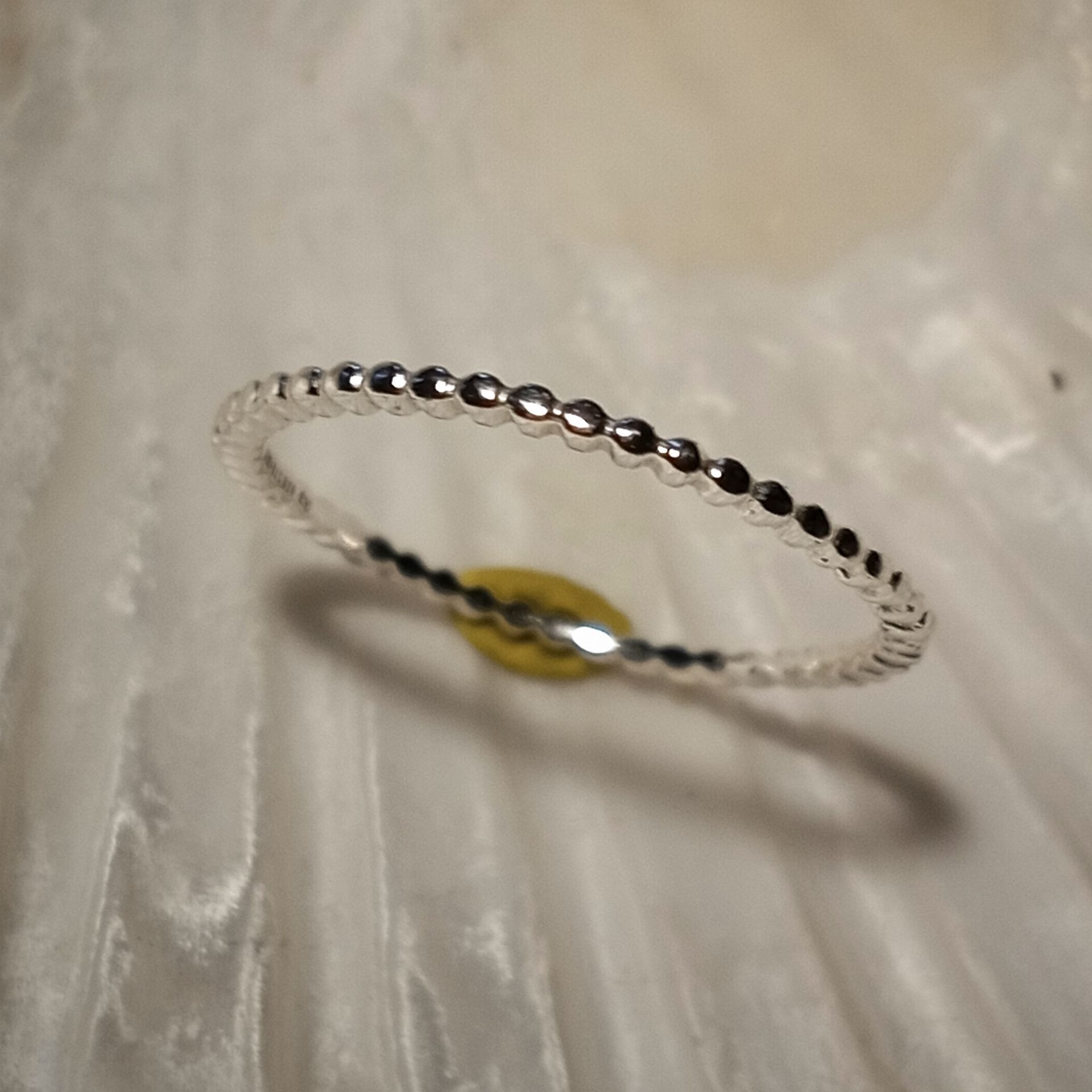 Silberner Perlenring auf weißem, strukturiertem Untergrund.