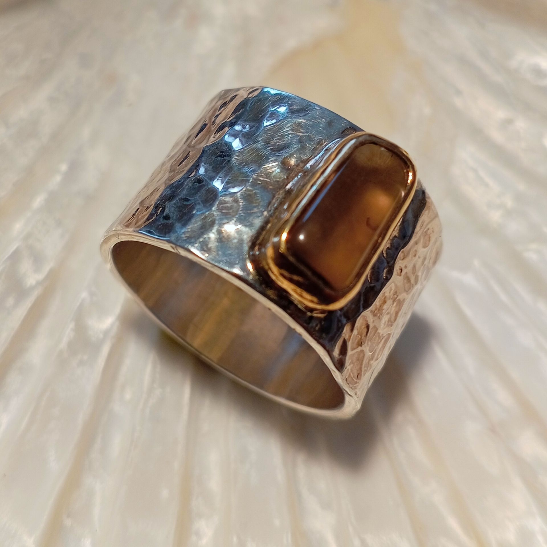 Silberring mit gehämmertem Muster und einem rechteckigen braunen Stein.