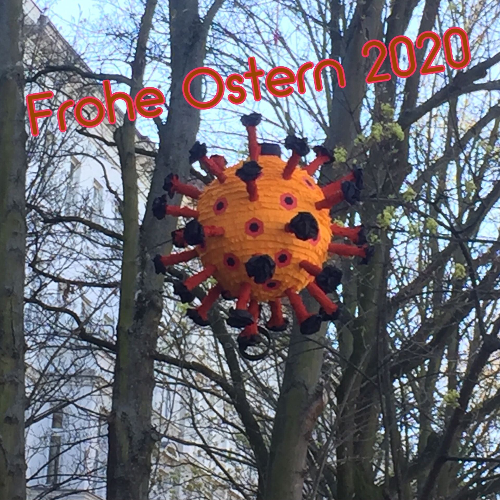 Orange corona virus piñata hanging in a tree, with 