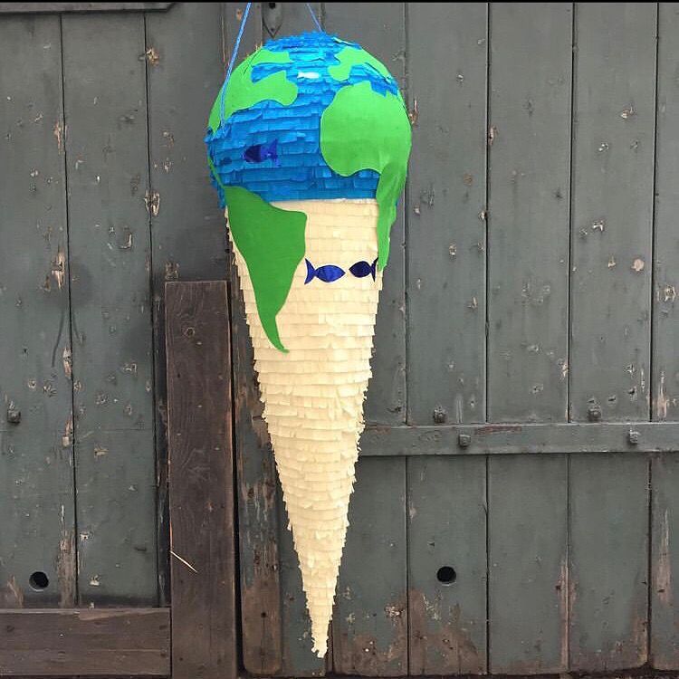 Eine erdförmige Piñata in Form einer Eistüte vor einer Holztür. Blau, grün und weiß.