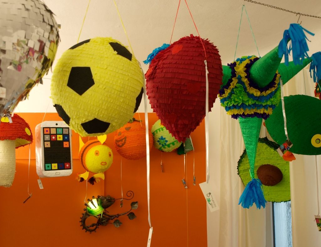 Verschiedene bunte Piñatas hängen von der Decke; ein Fußball, ein Herz und eine Eidechse sind zu sehen.
