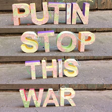 Bunte Pappbuchstaben bilden auf Betonstufen die Aufschrift „PUTIN STOP THIS WAR“.