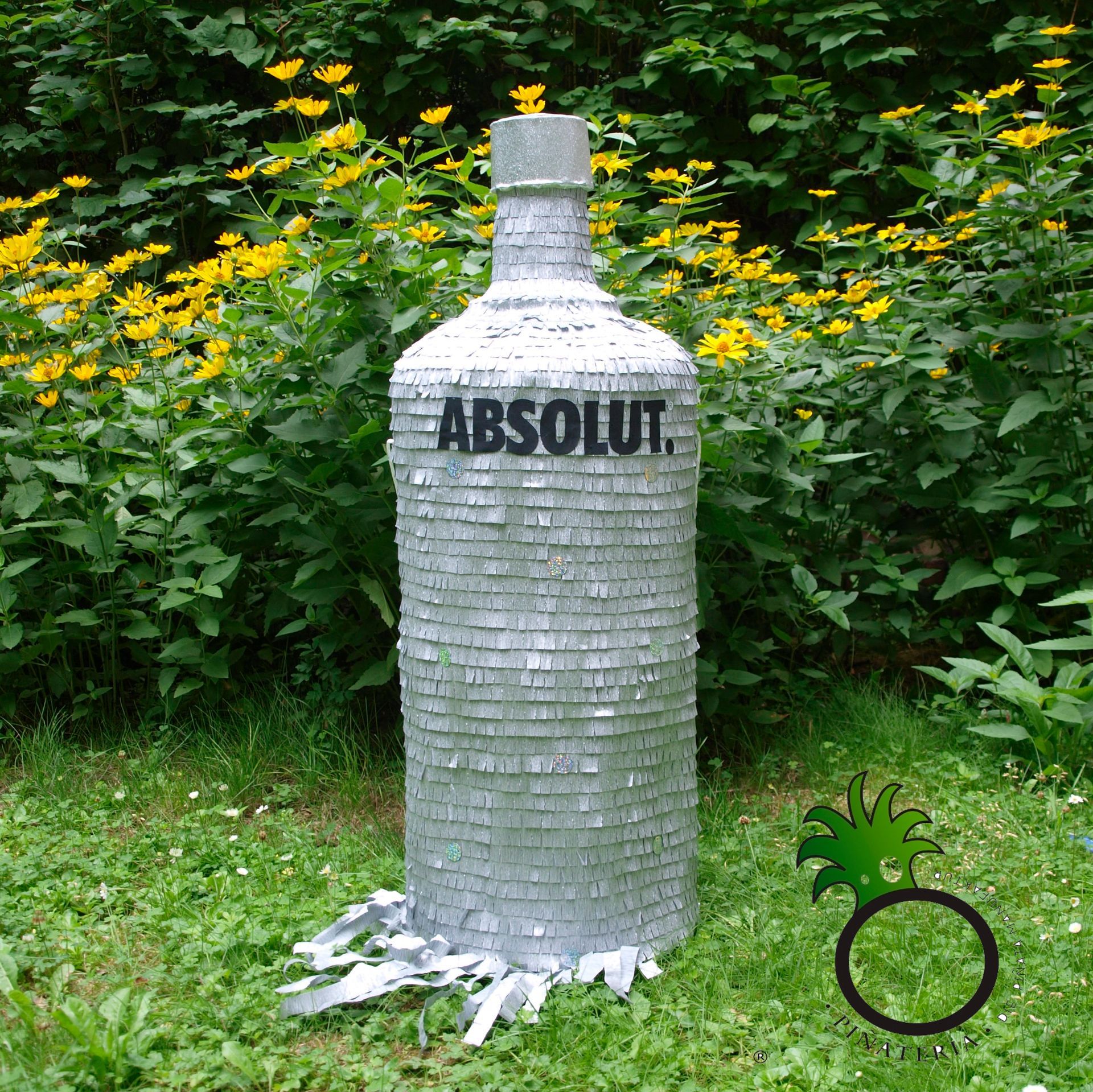 Große silberne Absolut Vodka-Flaschen-Piñata im Freien mit grünem Laub.