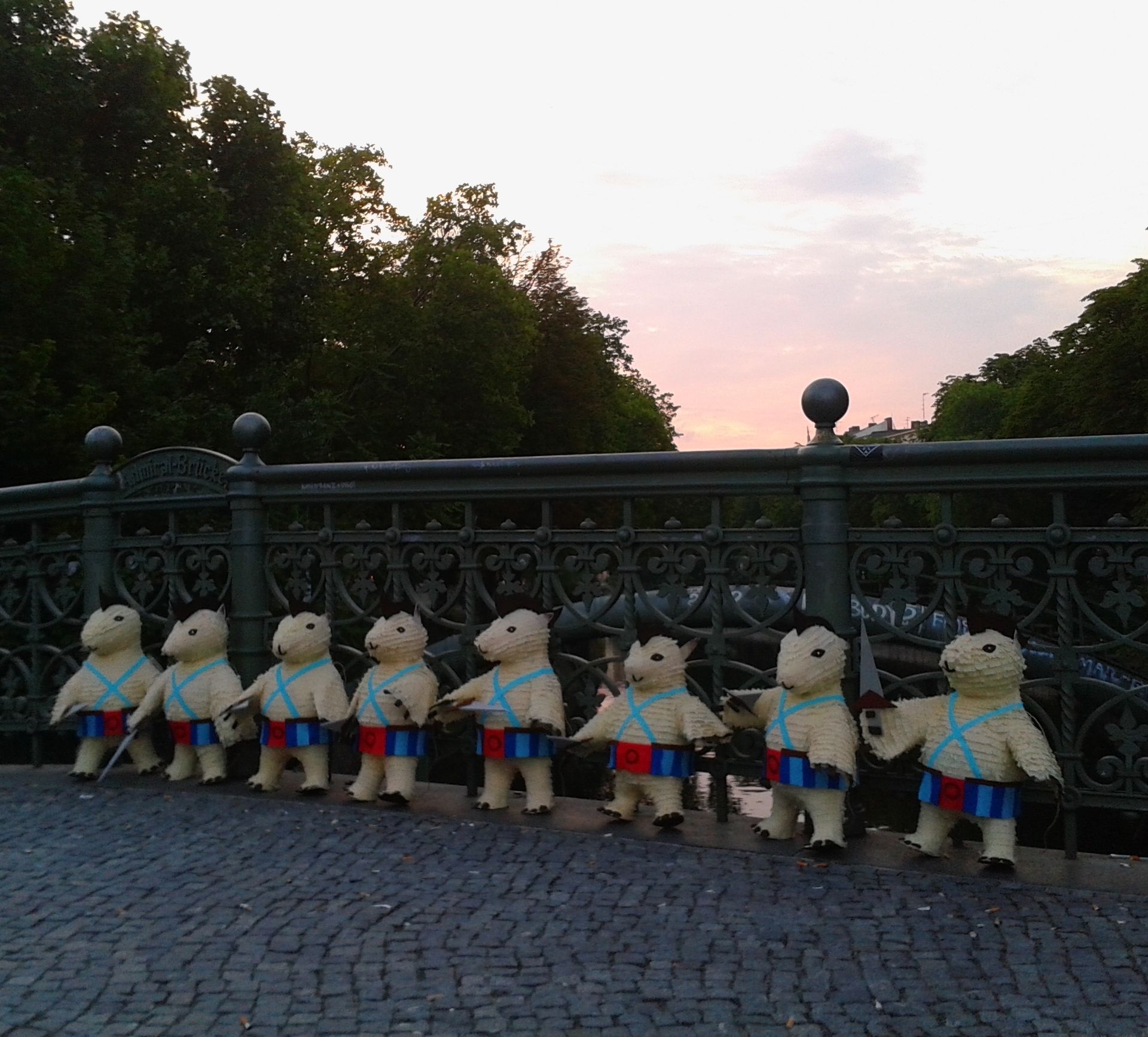Eine Reihe teddybärähnlicher Figuren in Kriegerkleidung auf einer Brücke in der Abenddämmerung.