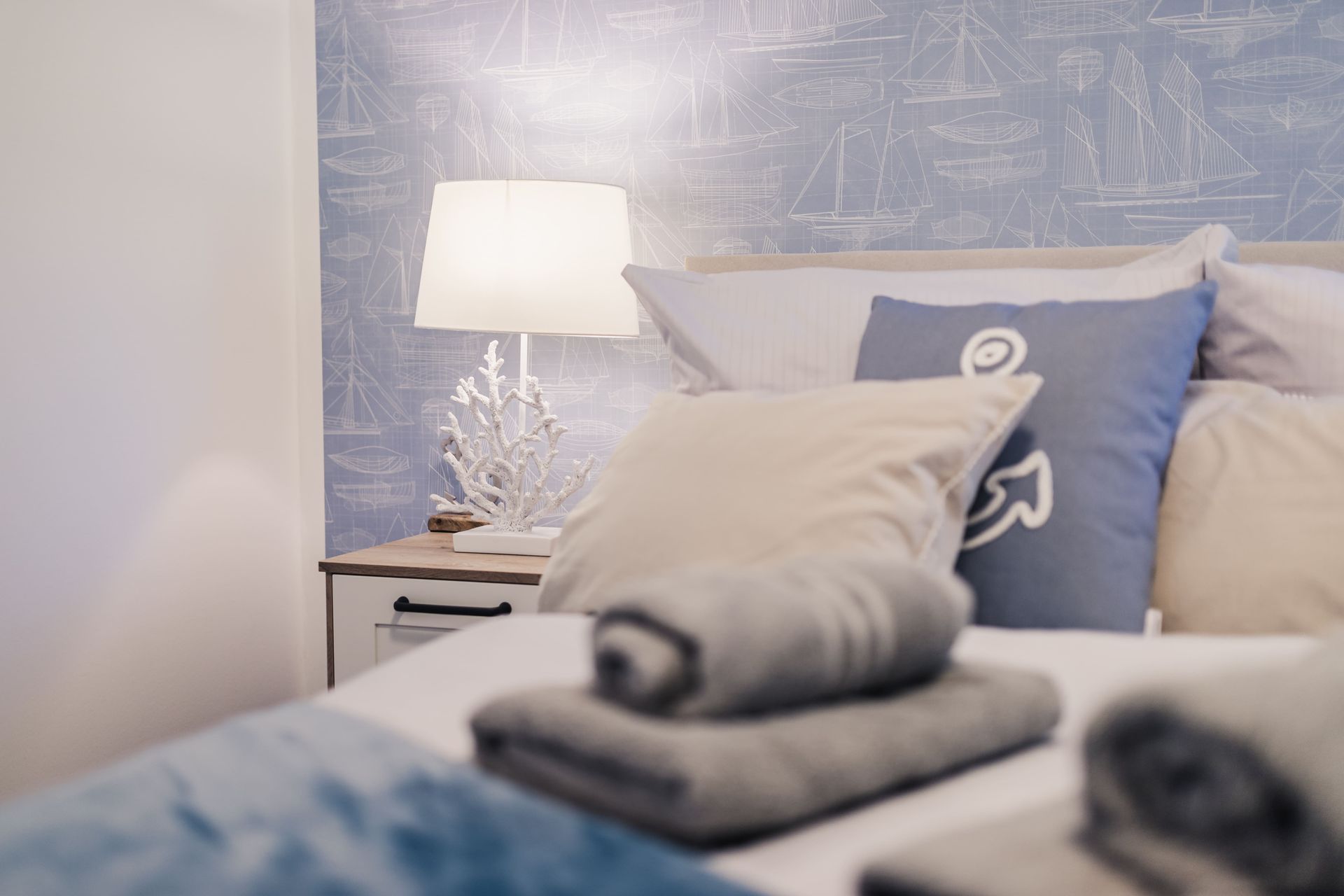 Bett mit Handtuchrolle und Nachtischlampe vor moderner Tapete