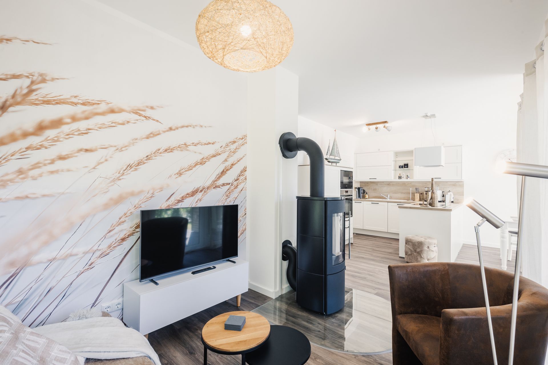 Wohnzimmer mit Flat-TV, Ofen und offener weisser Küche