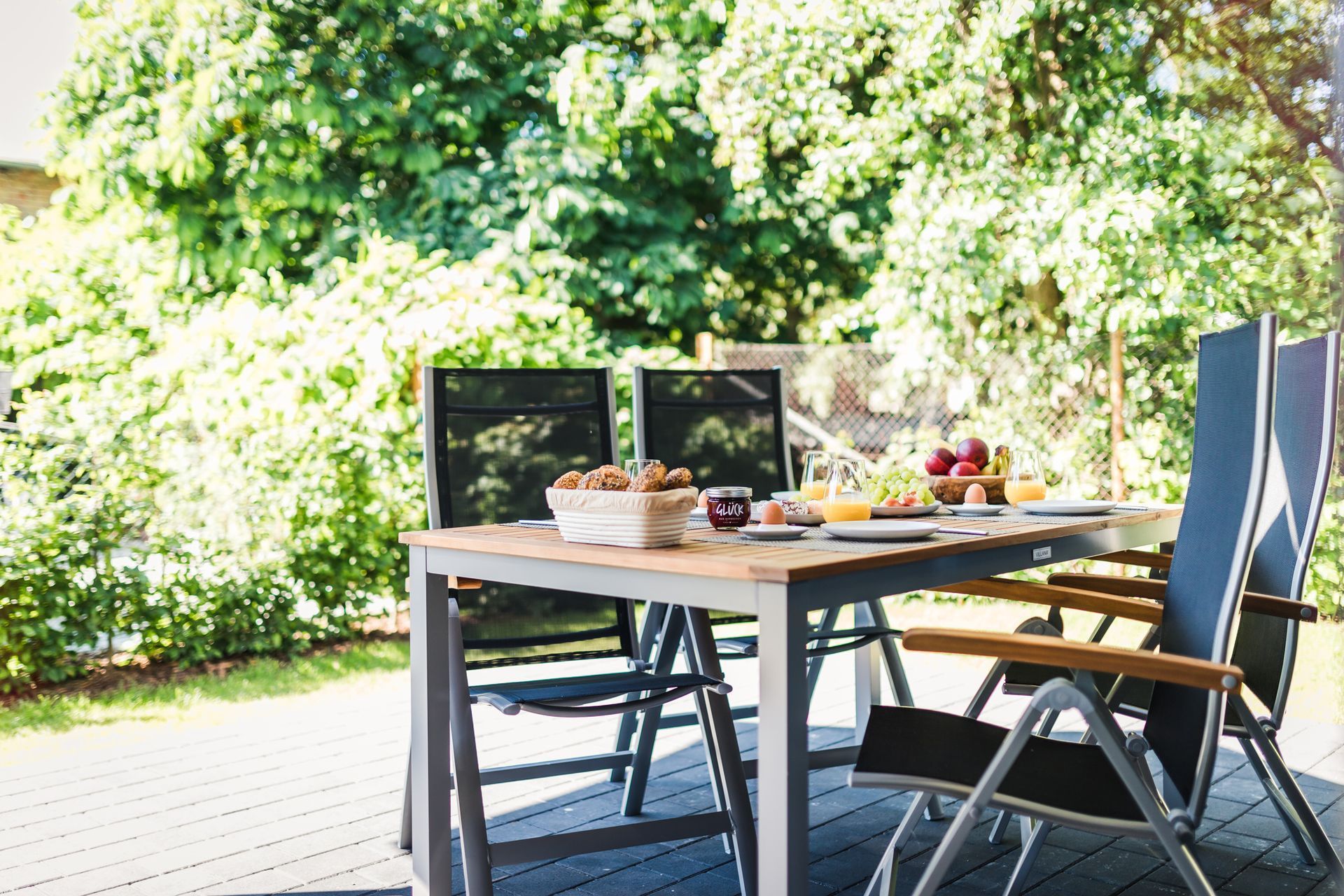 Blick von innen auf die Terrasse mit Tisch und Stühlen in den grünen Garten