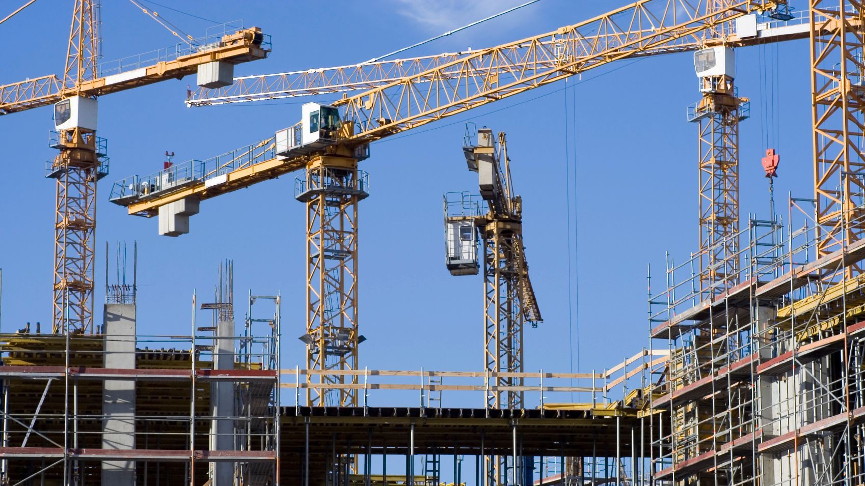 Baustelle mit gelben Kränen vor strahlend blauem Himmel. Gebäude im Bau.