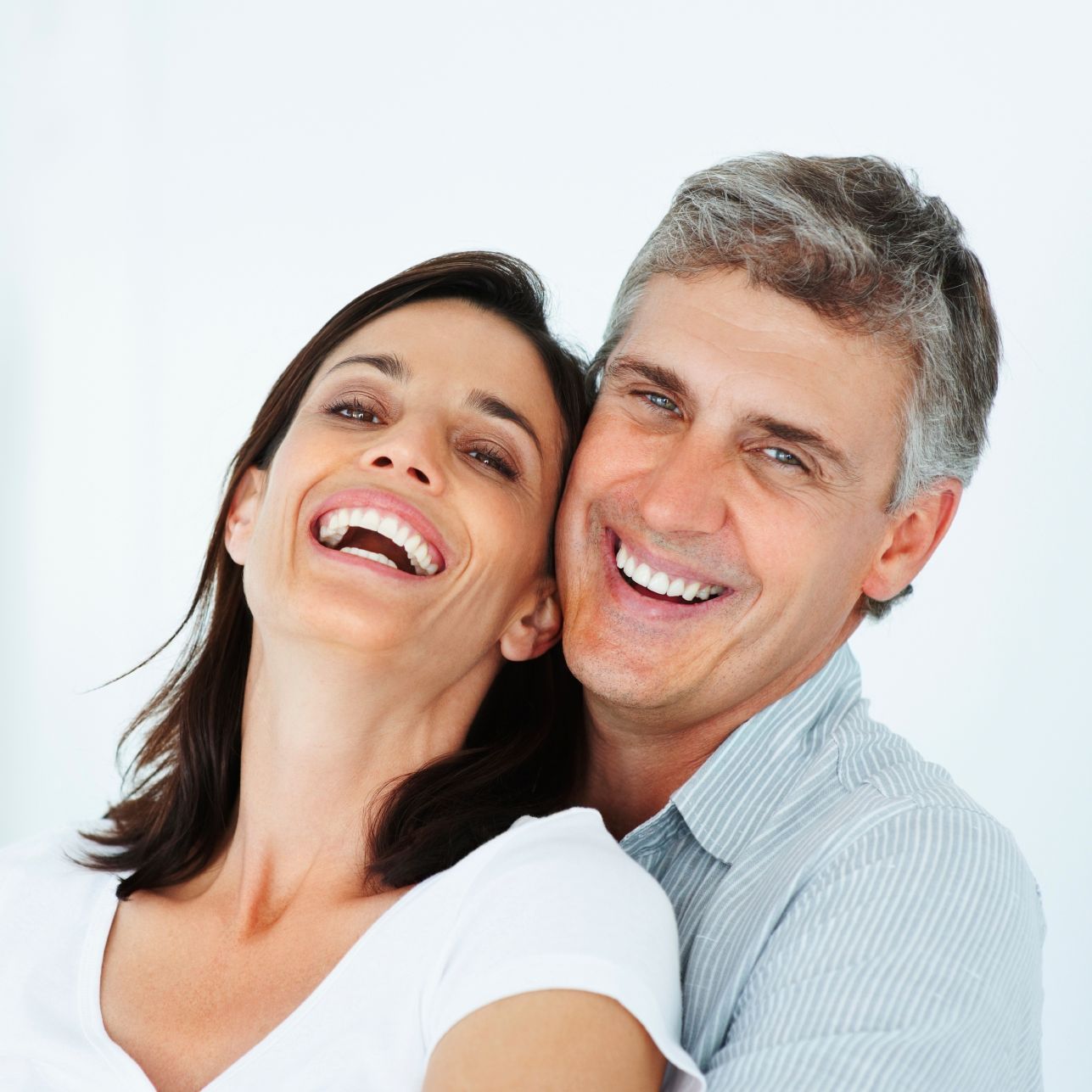 Lächelndes Paar, Frau lehnt Kopf an der Schulter des Mannes, beide mit weißen Zähnen, drinnen.