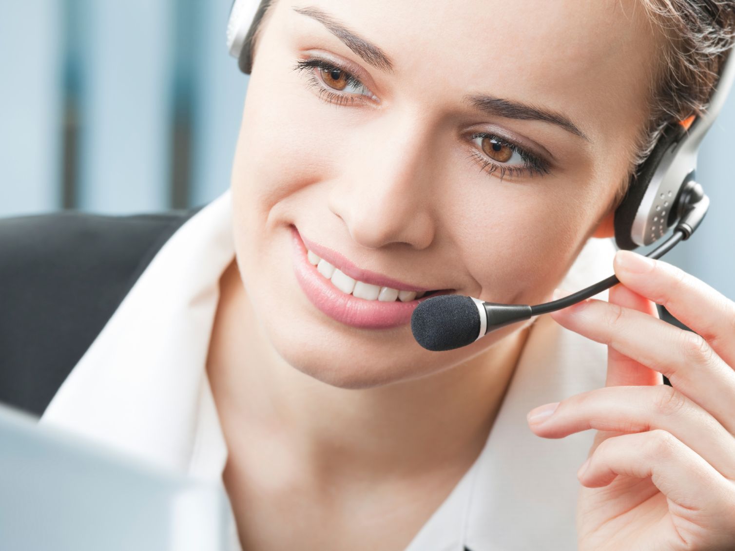 Frau mit Headset, die lächelt, während sie in einem Büro auf einen Computerbildschirm schaut.