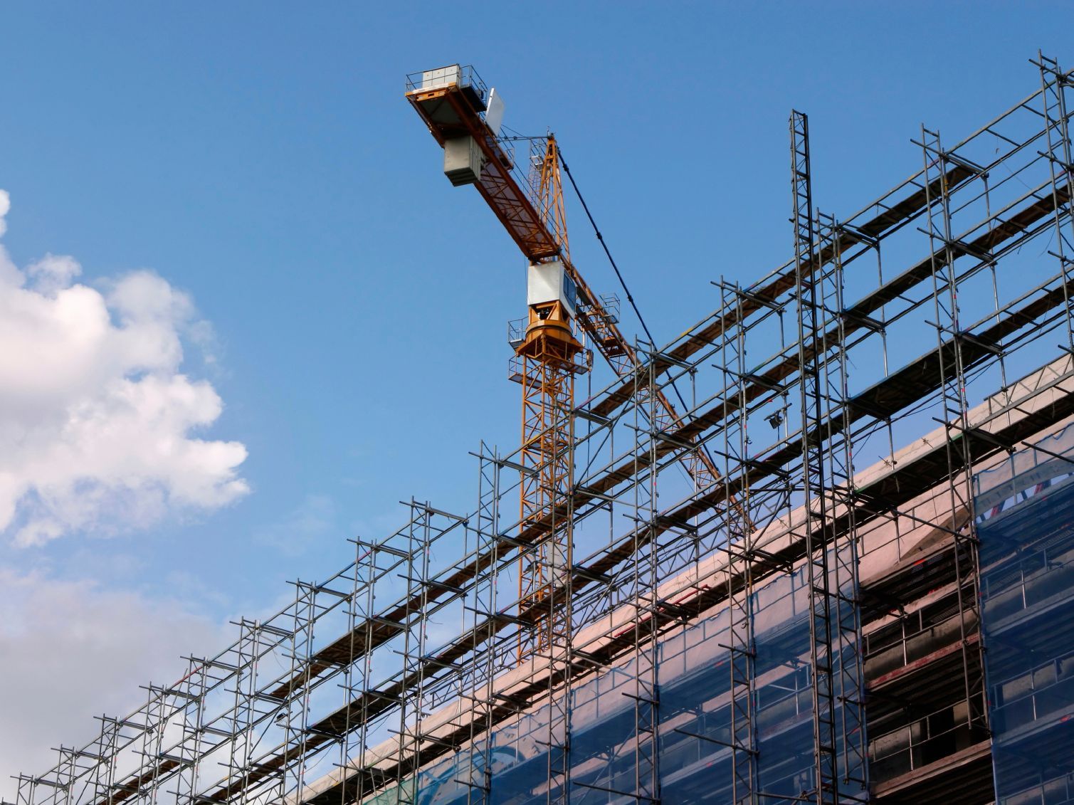 Baustelle mit Kran und Gerüst vor blauem Himmel.