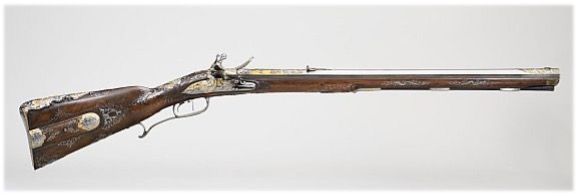 Ein antikes Gewehr mit Holzschaft und langem Lauf vor weißem Hintergrund.