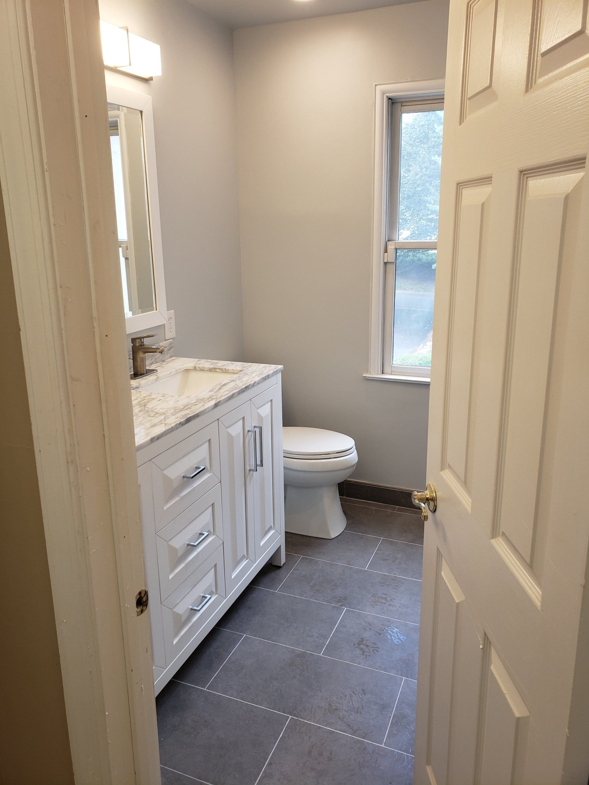 View of bathroom window, toilet, double sink vanity and modern style large format tile in elkins park bathroom remodel