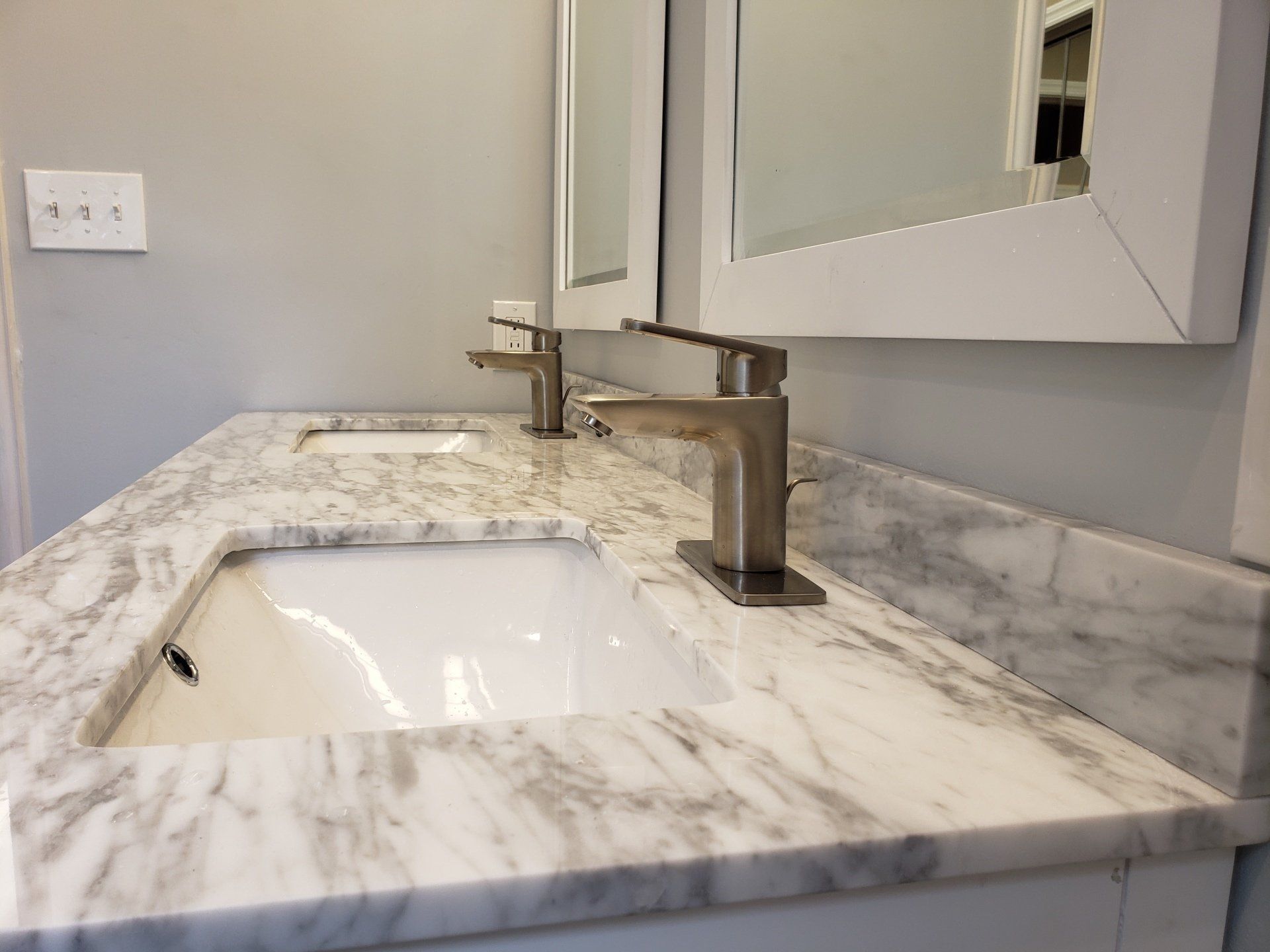 Close up of marble top and modern style faucets on double sink and double mirror vanity in elkins park bathroom remodel