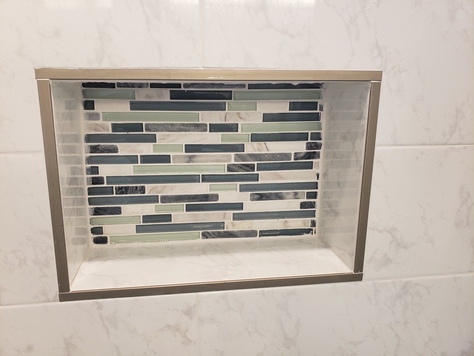 Close up of shower niche with interlocking glass tile accent colors of blue and light green