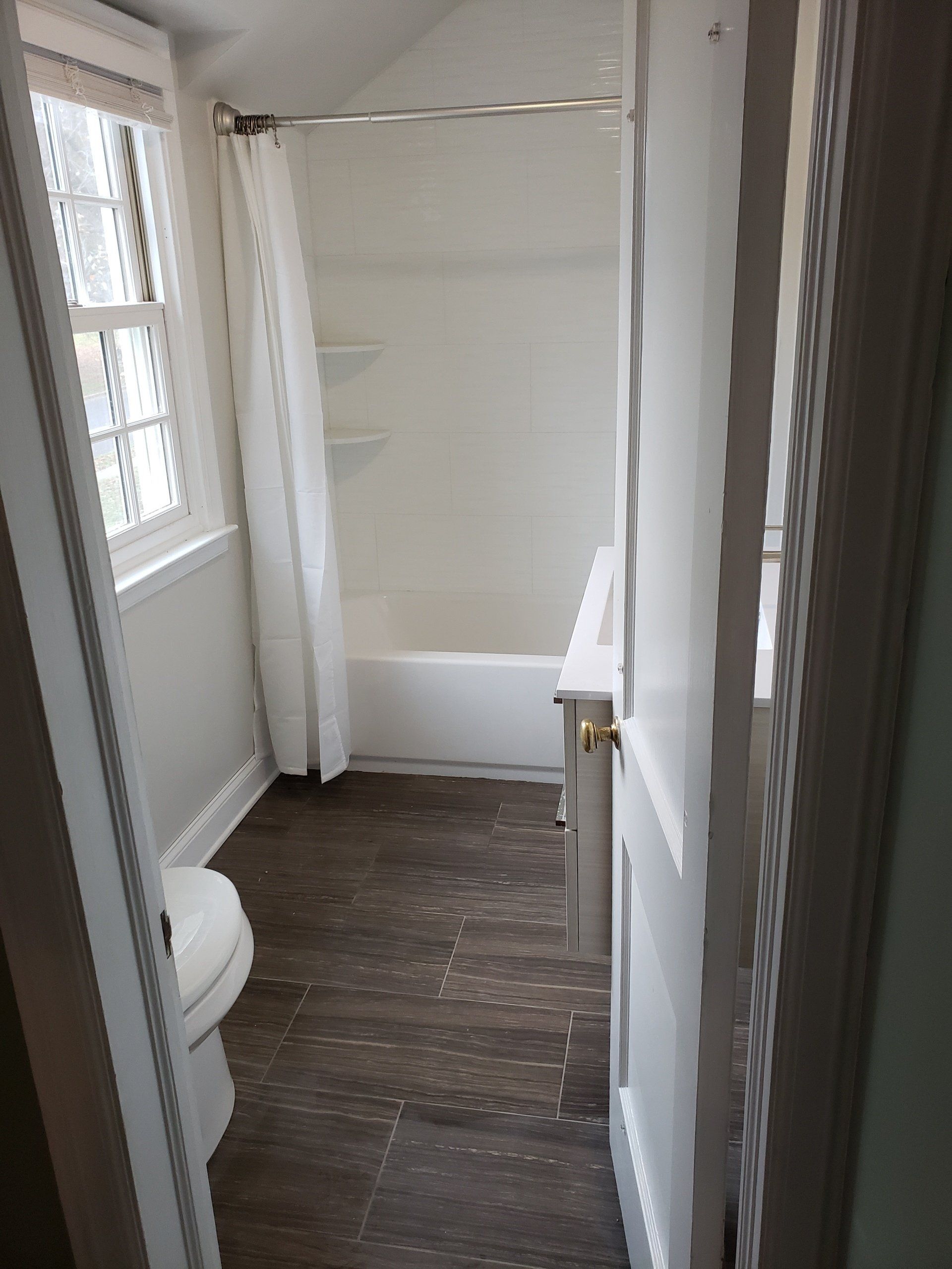 View of floor tiles, shower tiles, bathtub, wall paint and window in this bathroom remodel in Willow Grove.