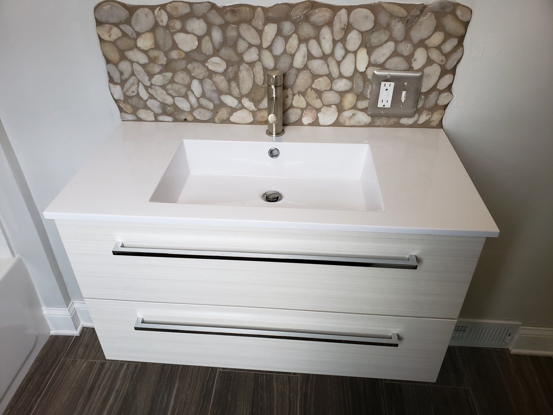 Front view close up of modern style floating vanity and sink with custom designed and installed pebble backsplash in Willow Grove master bathroom remodel.