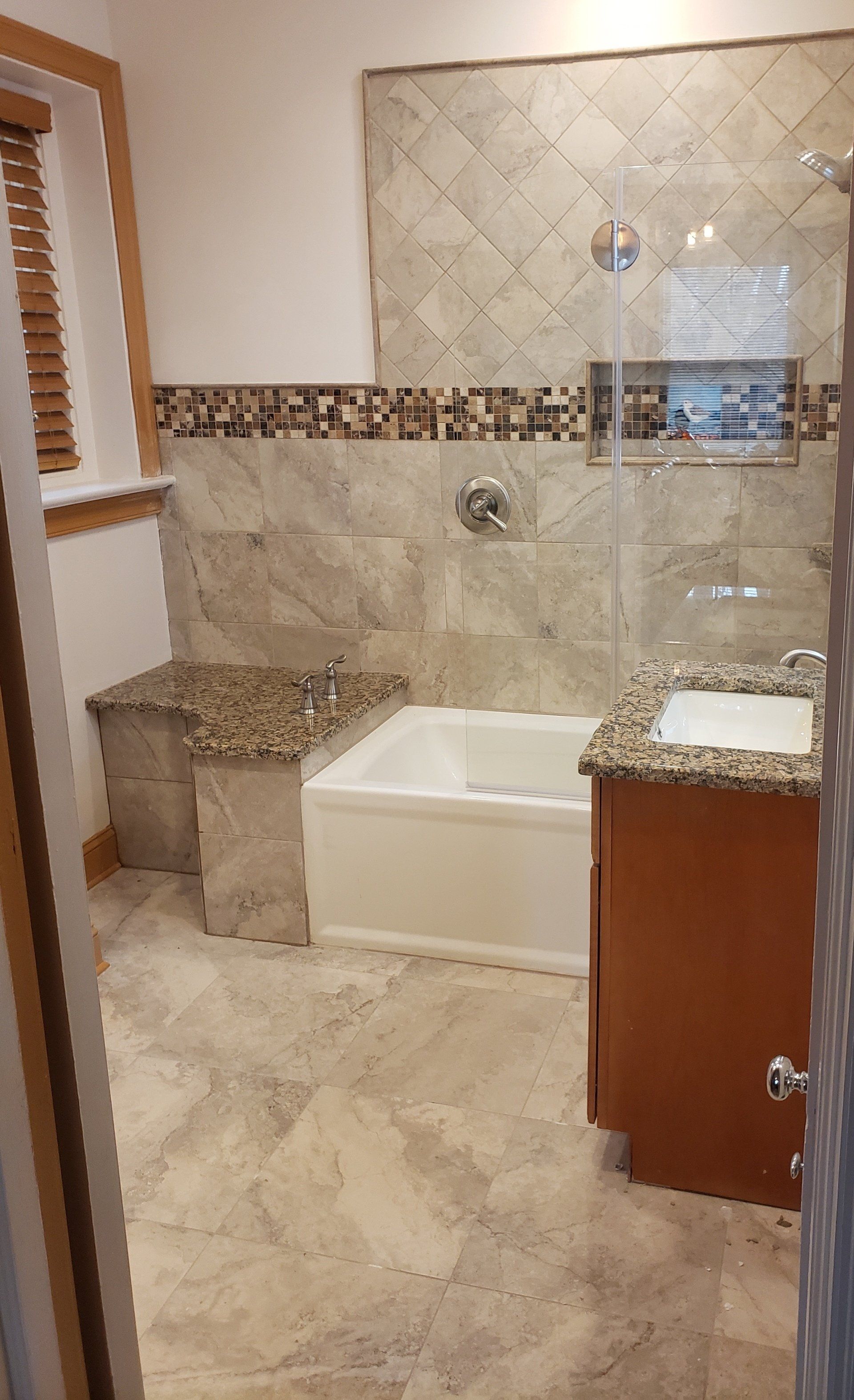 View of tiled wall, tiled floor, sink, custom bench, granite bench top and sink countertop, mosaic tile trim, pocket shelf in shower and accent painted tile in Cheltenham bathroom remodel.