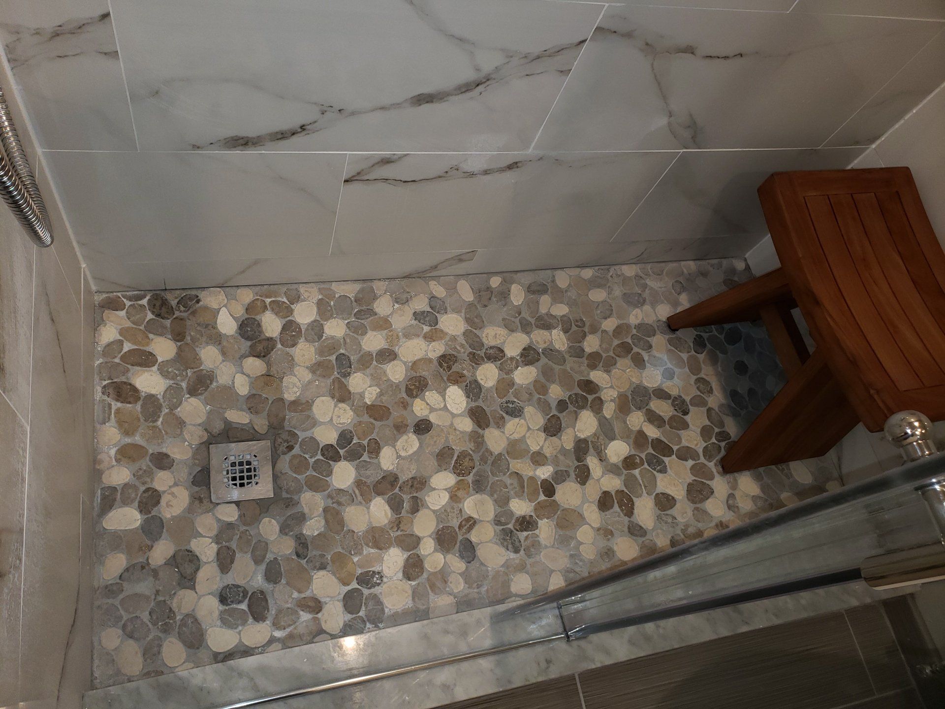 Pebble shower floor, witha wooden bench and marble shower tile in Jenkintown bathroom remodel