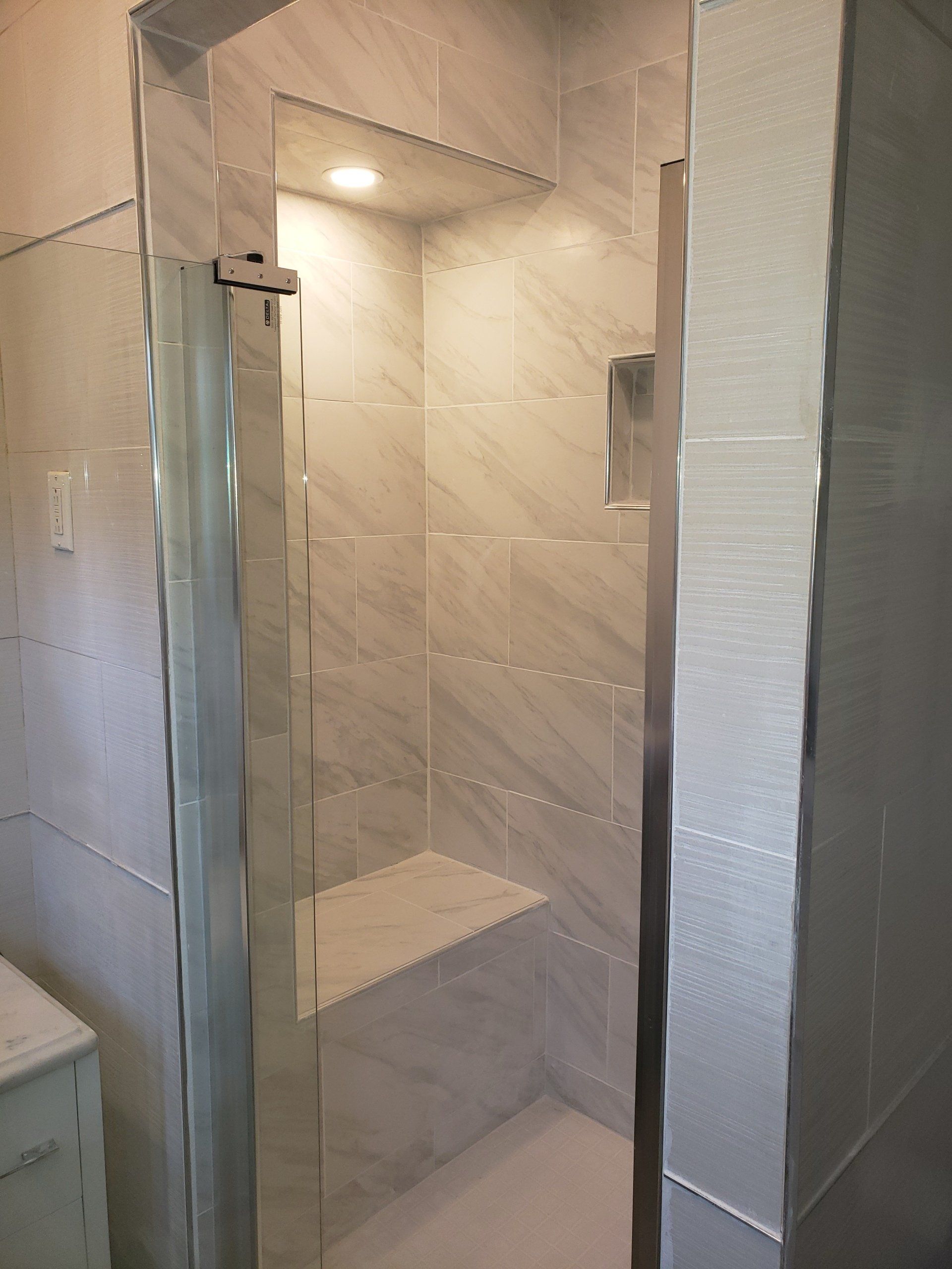 after photo of expanded and remodeled shower stall with a custom bench, pocket lights and floor to ceiling tile in Elkins Park.