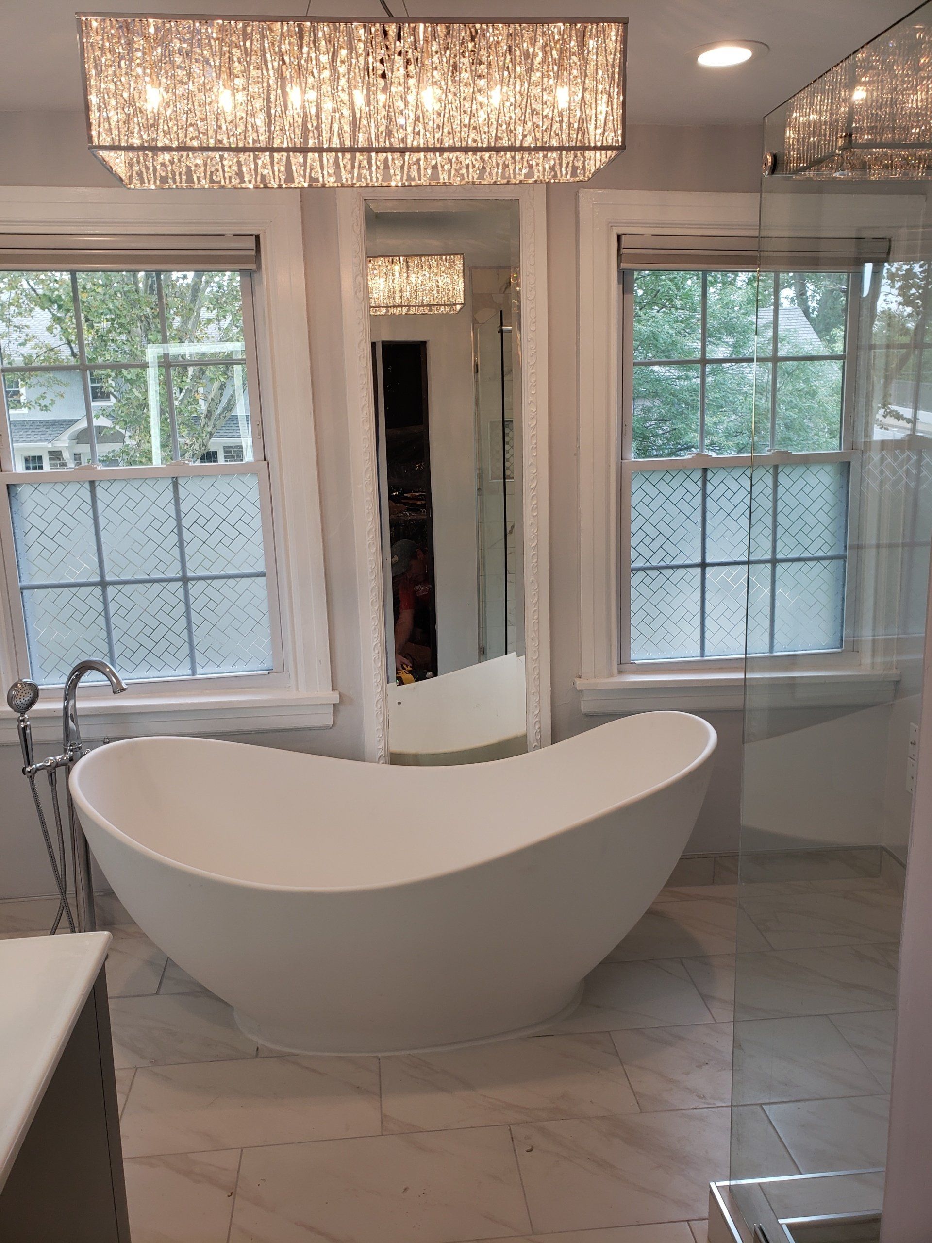 kidney shaped freestanding soaking tub and chandelier light fixture in master bathroom remodel in jenkintown