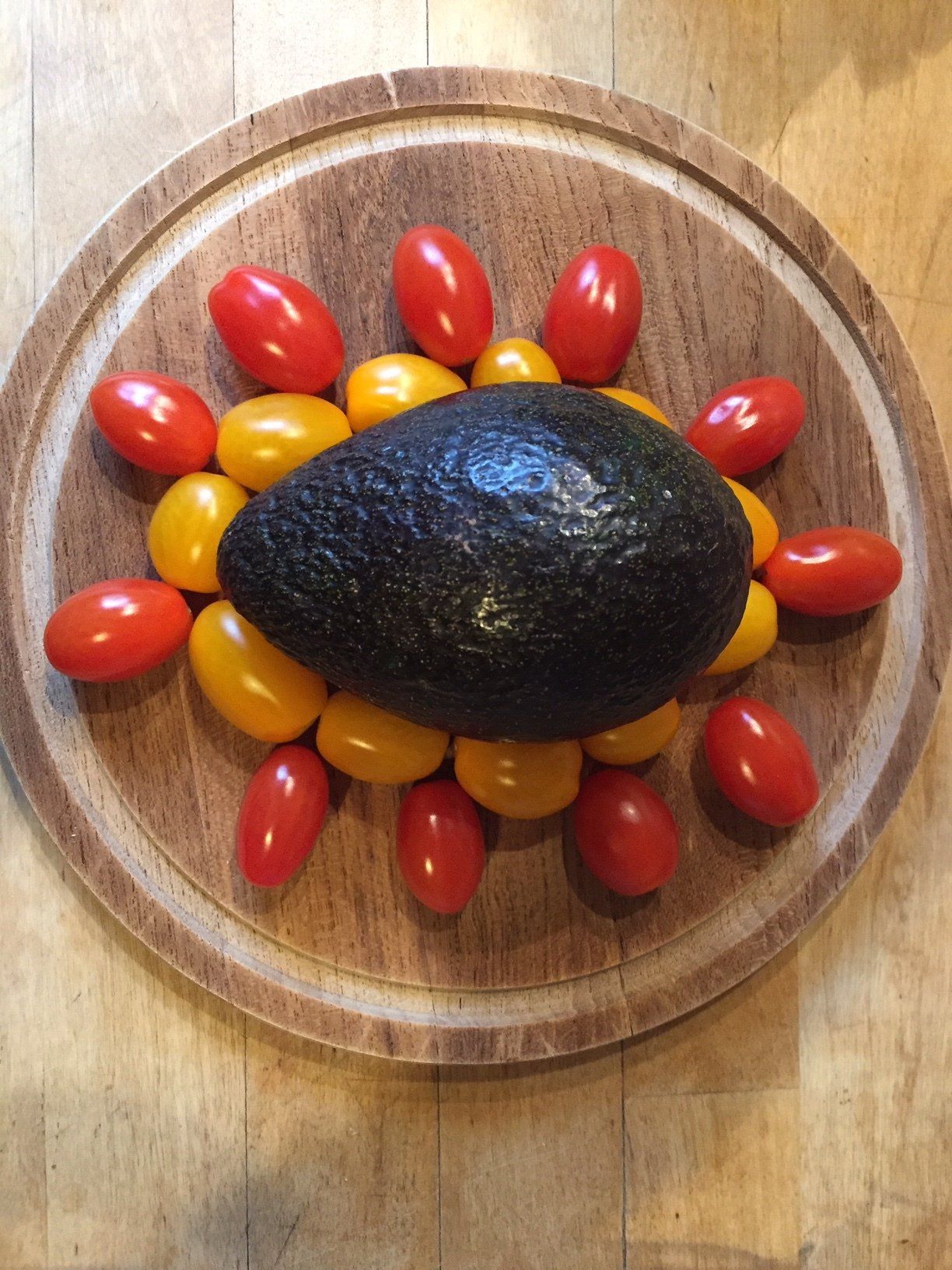 Eine Obstschale von oben. Darin: gelbe und rote Tomaten unn eine Avocado als Muster gelegt.