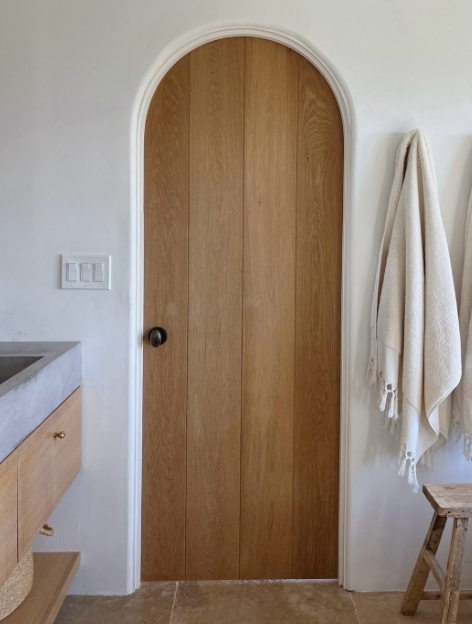 Puerta interior de madera natural con arco de medio punto y marco blanco, de inspiración mediterránea y andaluza.