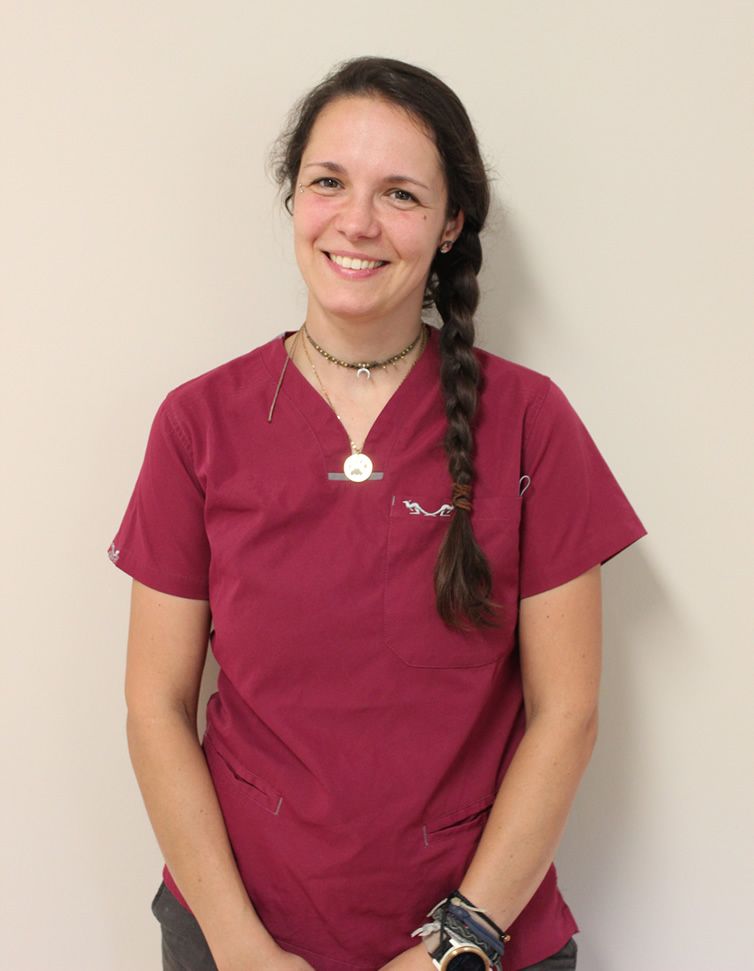 Hier sehen Sie Schwester Marie unsere medizinische Fachangestellt. Sie steht lachend vor einer hellbraunen Wand.