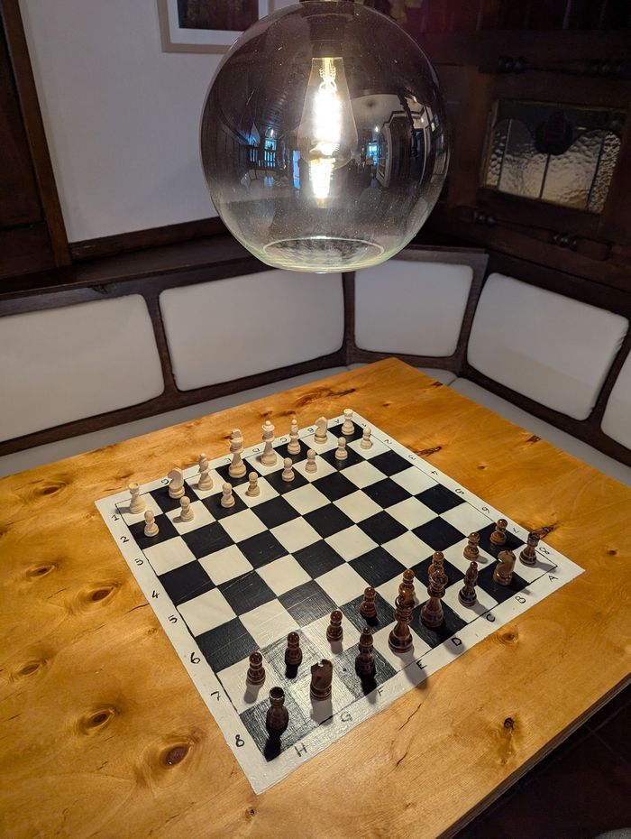Schachbrett im Holztisch unter einer warmen Pendelleuchte im Gambit