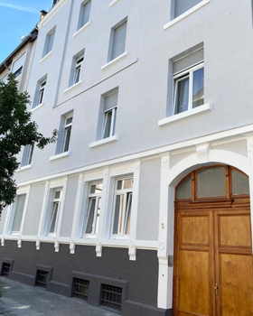 Hellgraue Fassade. Altbau. Weiße Fenster. Teakholztür.