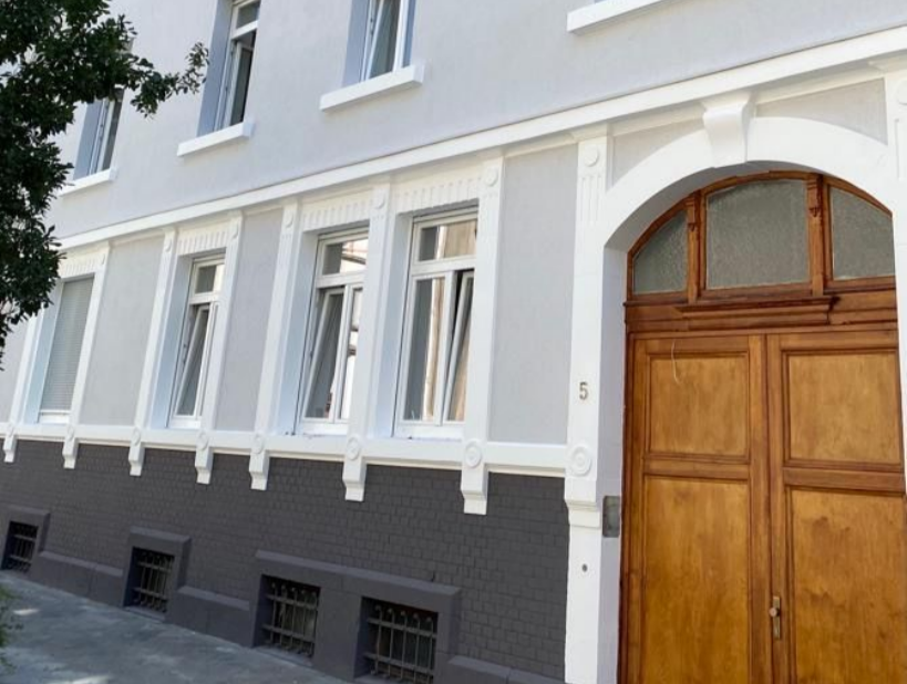 Hellgraue Fassade. Altbau. Weiße Fenster. Teakholztür.  