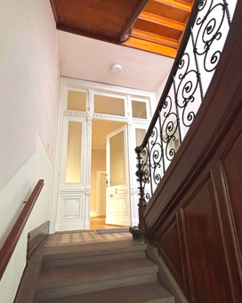 Altbau Treppenhaus. Weiße Eingangstür. Braune Holztreppe. Metallgeländer mit Schnörkeln.