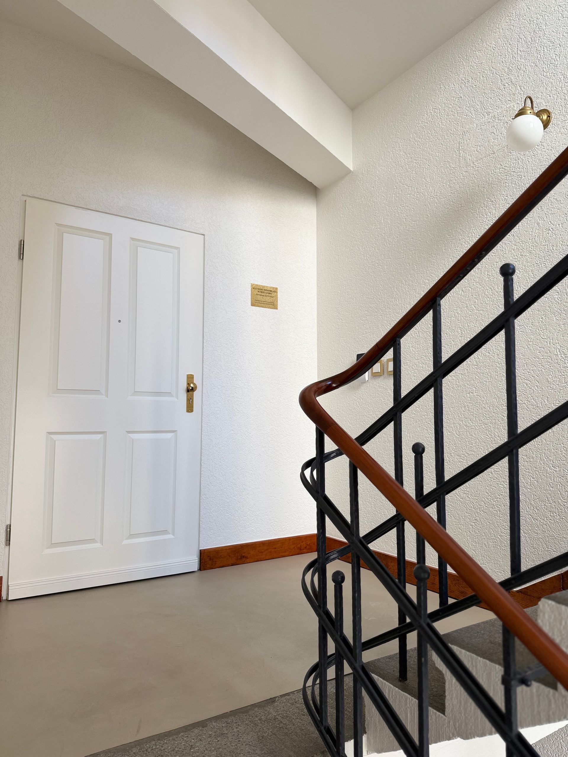 Weißes Treppenhaus Eingangstür. Altbau mit Metallgeländer und Holzhandlauf.