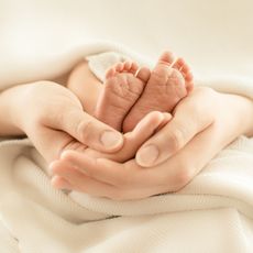 Hände einer Mutter, die die Füße ihres Babys halten.