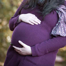 Bauch einer schwangeren Frau in einem beerenfarbenen Strickpullover.