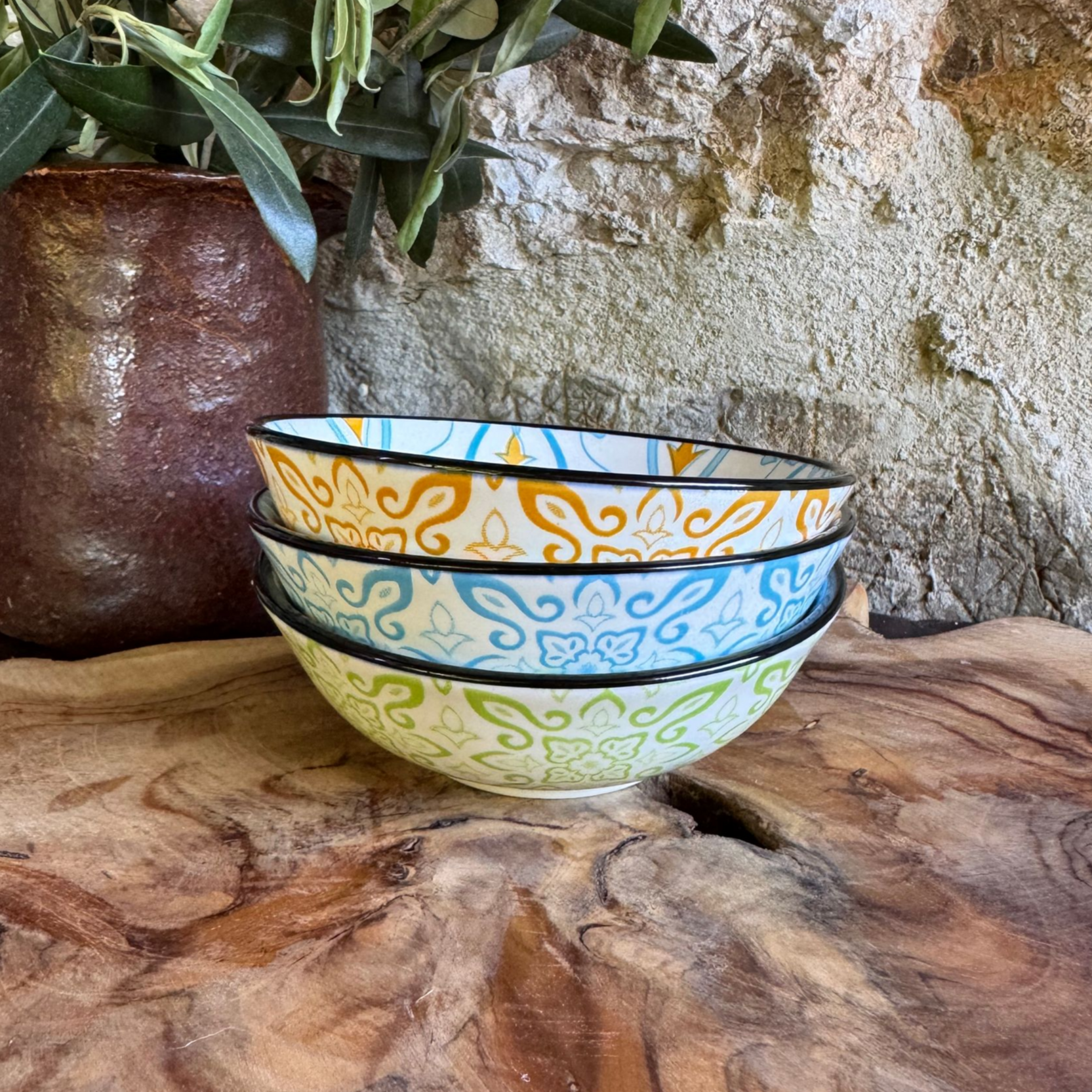 kleine, bunte Keramikschalen von außen in orangenem, blauem und grünem Muster auf einem Olivenholzbrett drapiert 