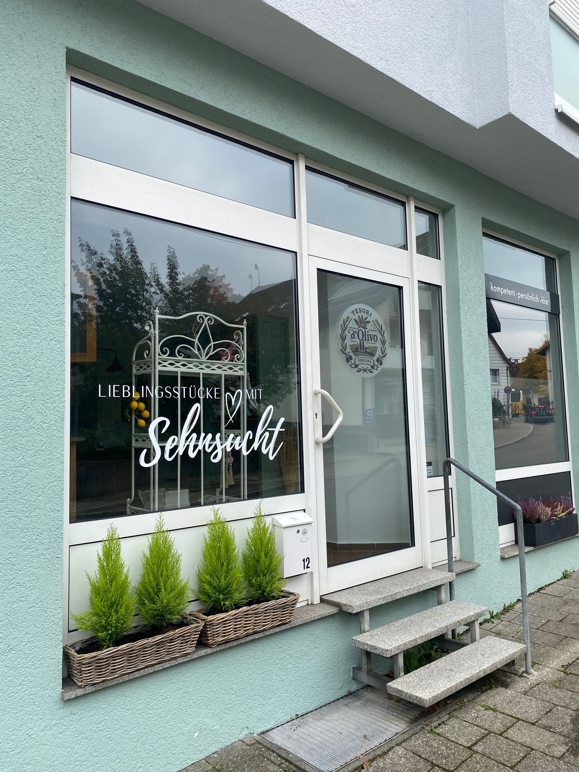 eine Glasfront mit weißem Rahmen und Tür und Beklebung, die die Außenansicht von Tesori d´Olivo darstellt