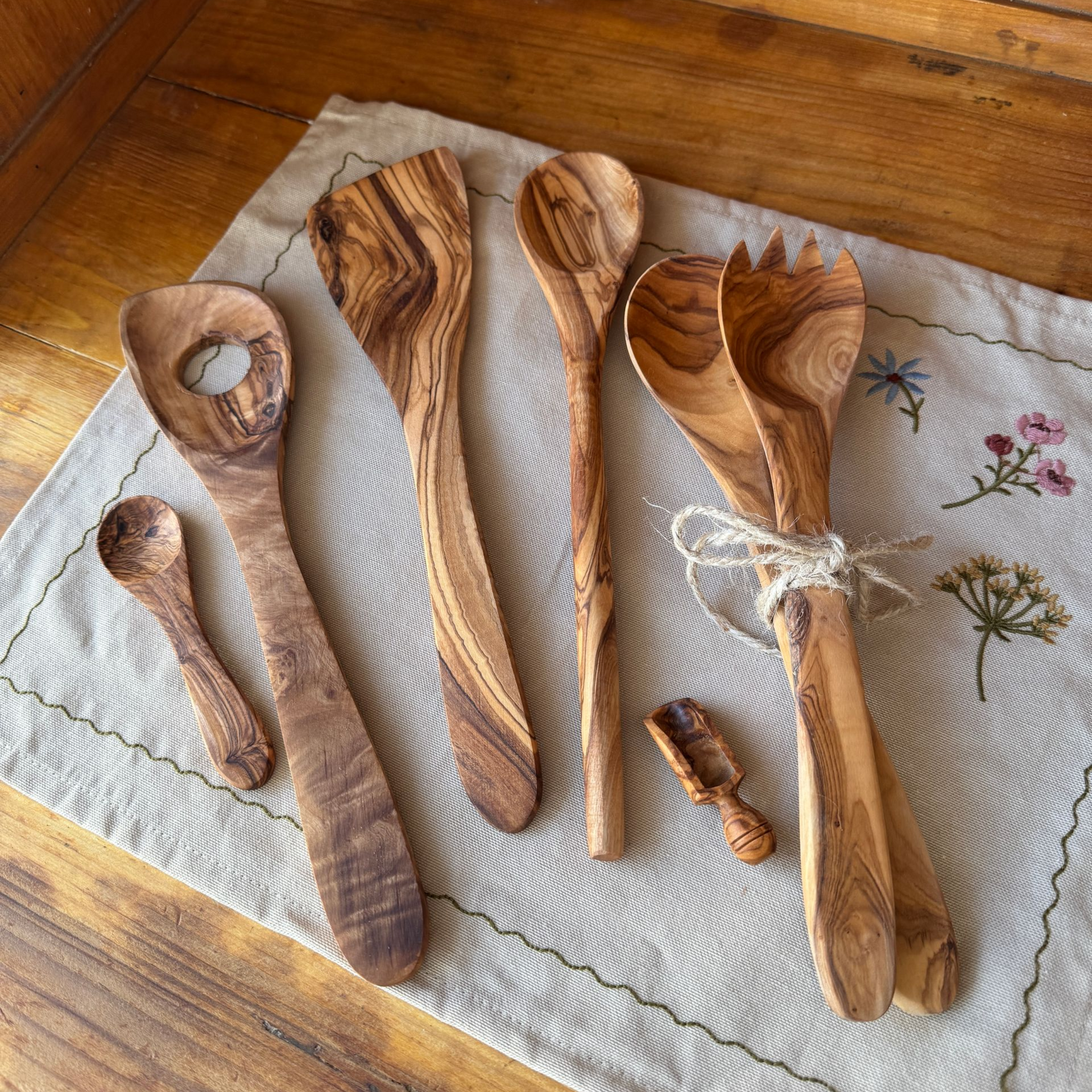 Salatbesteck, Kochlöffel, Pfannenwender, Risottolöffel, Dosierschäuffelchen und Teelöffel aus Olivenholz auf beigem Stoff