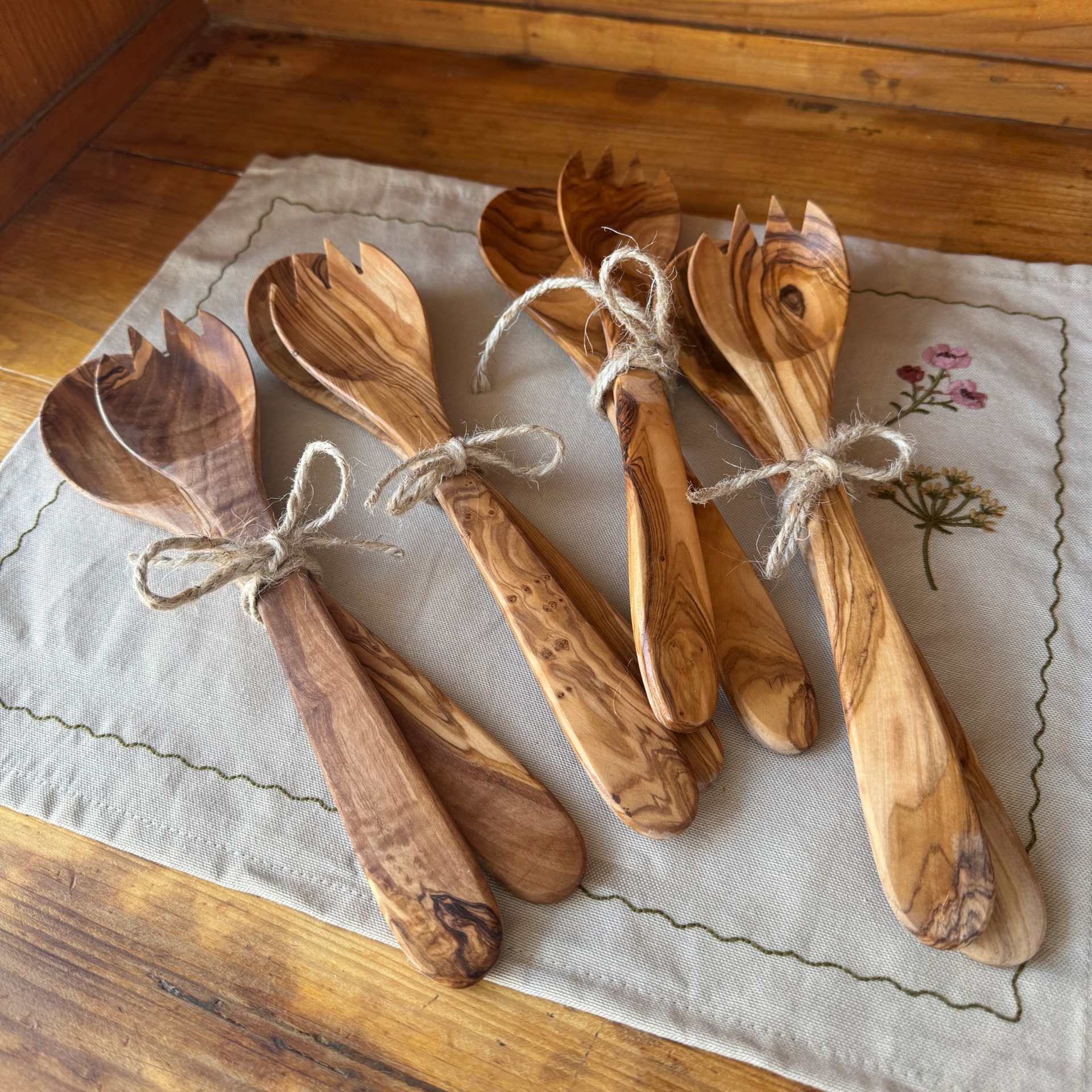 mehrere zusammengebundene Paare Salatbesteck aus Olivenholz auf einer mit Blumen bestickten naturfarbenen Stoffserviette