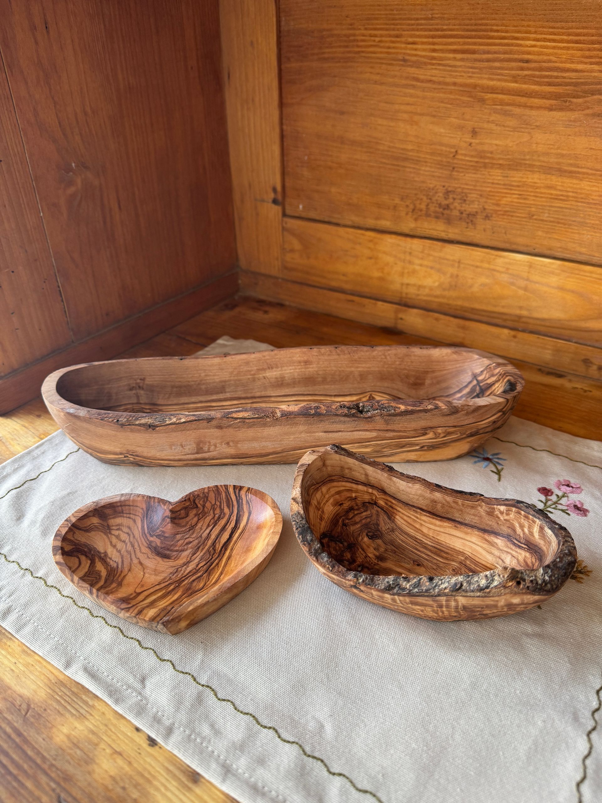 lange Olivenholzschale hinter einer kleineren Olivenholzschale und einer flachen herzförmigen Olivenholzschale