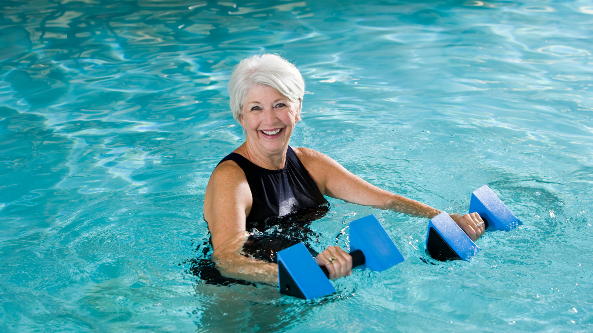 ältere Frau steht im Wasser mit 2 AquaFitness Hanteln in der Hand