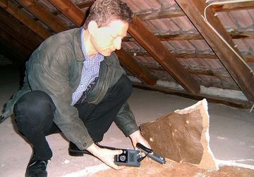 Baugutachter misst auf einem Dachboden mit einem Feuchtemessgerät. Link zu Feuchteschadenuntersuchung