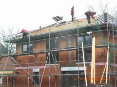 Einfamilienhaus mit Baugerüst, Bauarbeitern und Bausachverständigen auf dem Dach