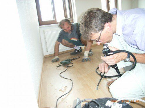 Bausachverständiger und Baugutachter sondieren mit Endoskop den Fußboden einer Wohnung
