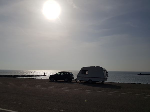 an der Nordsee: Abendstimmung, im Gegenlicht sieht man die Silouette eines Autos mit Wohnwagen am Strand