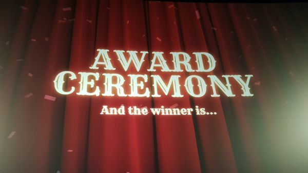 auf einen roten Vorhang sind die Worte projeziert: Award Ceremony, and the winner is...